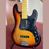 Elektrická basová kytara s korpusem v barevném přechodu od žluté přes oranžovou k červené a černé. Nástroj má černý pickguard, čtyři ovládací knofíky…