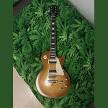 Elektrická kytara typu Les Paul v žlutohnědé barvě s hnědým přechodem. Na hlavě je nápis "Epiphone" a logo. Kytara má dva humbuckery, čtyři ovládací…