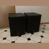 Dva černé reproduktory v hranatých bednách s přední kovovou mřížkou. Na spodní části obou reproduktorů je umístěno bílé logo a nápis behringer. Povrc…