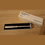 Bílý papírový obal a otevřená krabice s měřicím mikrofonem stříbrné barvy. Na obalu je nápis Full confidence in sound, Measurement Microphone a logo…