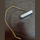 Na tmavé dřevěné desce leží černý magnetický snímač s chromovaným krytem a dvěma přilehlými šrouby. Ze snímače vycházejí dva dlouhé vodiče, jeden v č…