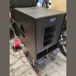 Černý aktivní subwoofer v hranatém korpusu s matným povrchem. Na horním pravém rohu je modro-bílé logo s nápisem MACKIE Active. Přední strana obsahuj…