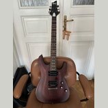 Elektrická kytara s tmavě hnědým, polomatným povrchem těla a hnedým hmatníkem. Na hlavě je bílý nápis Schecter Diamond Series. Nástroj má dva humbuck…