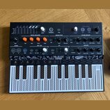 Černý kompaktní syntetizátor s nápisem MICROFREAK SYNTHESIZER. Horní panel obsahuje různé ovládací prvky, knoflíky a nápisy jako DIGITAL OSCILLATOR,…