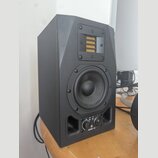 Černý studiový monitor v hranaté skříni. V horní části je umístěn páskový výšek s žlutým membránovým prvkem, uprostřed je kruhový střední reproduktor…