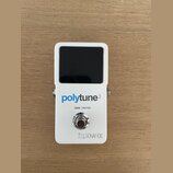 Bílý kytarový tuner s černým displejem. Na přední straně je modrý a šedý nápis polytune3, pod ním text TRUE | BUFFER a ve spodní části logo s nápisem…