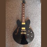 Černá polodupatá elektrická kytara s lesklým povrchem a hnědým hmatníkem. Na hlavě je nápis Epiphone, na krytkách snímačů a mostu jsou zlaté prvky. K…