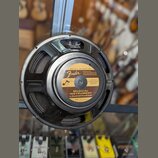 Kruhový reproduktor v černém plastovém rámu. Na středovém krycímu krytu je hnědý štítek s nápisy „specially designed for Fender MUSICAL INSTRUMENTS C…