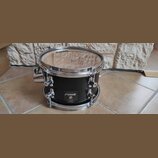 Černý buben s chromovaným obručováním a mechanismy. Na korpusu je nalepený štítek s nápisy SONOR, Sonic Rain a MADE IN GERMANY. Na horním blaně je vi…
