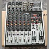 Stříbrný mixážní pult značky behringer s černým šasi. Na horním panelu je nápis 2-TRACK/USB a modelové označení XENYX X1204USB. Zařízení obsahuje něk…