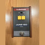 Šedý efekt pedál s dřevěným rámem a červeným horním panelem. Na zařízení jsou nápisy tc electronic, MONO, STEREO, I, II, JUNE-60, CHORUS a TRUE BYPAS…