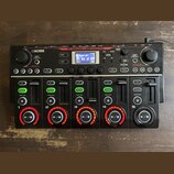 Černý loop station Boss RC-505mkII. Zařízení má digitální displej, řadu tlačítek a pět sekcí s posuvníky a ovládacími knoflíky. Na horní části je náp…
