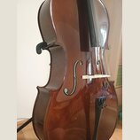 Detailní pohled na hnědý lakovaný smyčcový nástroj, pravděpodobně violoncello. Na těle jsou vidět dvě f-otvory a bílý kobylík, přes který vedou čtyři…