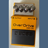 Žlutý efekt pedál s kovovým horním panelem a čtyřmi chromovanými oválnými knoflíky. Na přední straně jsou nápisy OUTPUT, INPUT a velký text OverDrive…