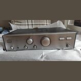 Stříbrný integrovaný stereo zesilovač s černým horním krytem a ventilační mřížkou. Na předním panelu jsou nápisy ONKYO, INTEGRATED STEREO AMPLIFIER a…