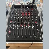 Černý DJ mixér s mnoha ovládacími prvky, potenciometry a posuvníky. Na panelu jsou viditelné nápisy jako MASTER, FILTER, CUT / BOOST, CUE A, CUE B a…