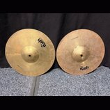 Dvě mosazné činely s viditelným opracováním povrchu. Oba mají nápis 13" Cymbal a logo flash CYMBALS. Povrch pravého činele vykazuje více drobných skv…