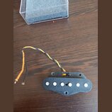 Černý elektrický snímač s šesti bílými póly, umístěný v černém plastovém rámečku. Ze snímače vedou dva kable, jeden žlutý a jeden černý, které jsou v…