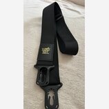 Černý textilní popruh na hudební nástroj s plastovými koncovkami. Na středním čtvercovém poli je žlutý nápis ERNIE BALL. Povrch popruhu i plastových…