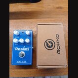 Modrý efekt pedál s nápisy "Rocket" DISTORTION a GOKKO. Na horní straně jsou čtyři bílé ovládací knoflíky s popisky VOLUME, GAIN, BASS, MID a TREBLE.…