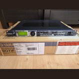 Černý rackový zvukový modul Yamaha Motif-Rack ES umístěný na originální kartónové krabici s nápisy YAMAHA CORPORATION a MOTIF. Na předním panelu je d…