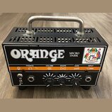 Černý kompaktní kytarový zesilovač s kovovou rukojetí nahoře. Na předním panelu je bílý nápis ORANGE a model Micro Dark. Zařízení má čtyři ovládací p…