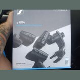 Fotografie znázorňuje krabici od mikrofonů s nápisy e 604 a Instrument Microphones. Na obalu jsou zobrazeny tři černé mikrofony s logem SENNHEISER a…
