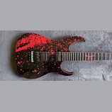 Elektrická kytara s černým povrchem a červenými stříkanci. Na hmatníku je vidět červený znak ve tvaru hvězdy a na kobylce nápis FLOYD ROSE. Kytara má…