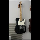 Černá elektrická kytara typu Telecaster s bílým pickguardem a světlou hmatníkovou deskou. Nástroj vykazuje známky opotřebení v podobě odlakování na s…