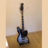 Čtyřstrunná basová kytara s černým korpusem a modrým přechodem v centru. Na hlavě je bílý nápis "Super Jazz Bass" a logo znázorňující kytaru. Nástroj…