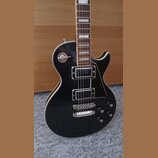 Černá elektrická kytara typu Les Paul s bílým lemováním. Na krytce horního snímače je nápis "Les Paul". Kytara má dva humbuckery, čtyři ovládací knof…