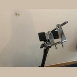 Chromovaná kovová držák na noty s dvěma černými gumovými plochami. Na utahovacím šroubu je viditelný nápis LOCK. Povrch je lesklý, s mírnými odlesky…