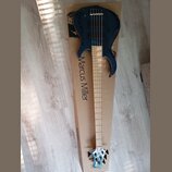 Tmavě modrá elektrická basová kytara položená na kartonovém obalu. Na obalu je svisle napsán text Marcus Miller. Hmatník je zC světlého dřeva a hlava…