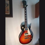 Elektrická kytara s tvarem singlecut a barevným přechodem od černé k oranžové. Na hlavě hmatníku je nápis "Gibson" a pod ním text "LES PAUL MODEL". N…