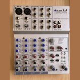 Stříbrný mixážní pult s nápisem ALTO L-6 6-CHANNEL MIXING CONSOLE WITH DIGITAL EFFECTS. Horní panel obsahuje vstupy MIC 1 a MIC 2, AUX SENDS, CONTROL…