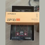 Kartonová krabice s nápisy Roland, DAMPER PEDAL DP-10 a Roland Corporation. Pod krabicí je vidět obal s produktem Line 6 POD Express, který obsahuje…