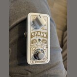 Bílý efekt pedál Spark Mini Booster značky tc electronic. Na přední straně je bílý oválný ovládací knoflík a stomečový spínač True Bypass. Jsou zde n…