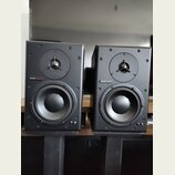 Dva černé studiové monitory v hranatých skříních. Na obou je umístěn nápis dynaudio acoustics. Každý reproduktor má v horní části výšek s kovovou mří…