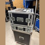 Dvě černé transportní bedny z překližky s černým povrchem a hliníkovými hranami a rohy. Horní bedna má na vrchu bílý štítek s nápisem "TOWNSIGHTER".…