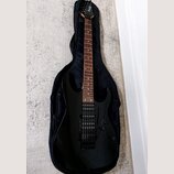 Černá elektrická kytara s tmavým hmatníkem, umístěná v černém poloměkém pouzdře. Na hlavě kytary je bílý nápis Ibanez. Nástroj má dva humbuckery, ovl…