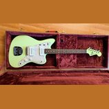 Světle zelená elektrická kytara v hnědém tvrdém kufru s purpurovým polstrováním. Kytara má bílý perleťový pickguard a na hlavě je nápis WOLF DupliTon…