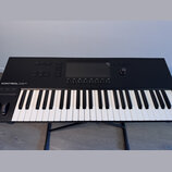 Černý MIDI kontrolér s klávesnicí umístěný na černém stojanu. Na horním panelu je nápis KONTROL S49 MK3, displej a řada ovládacích tlačítek a otočnýc…