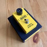 Žlutý efekt pedál MXR micro chorus umístěný na tmavomodré krabici. Na horní straně je černý ovládací knoflík s nápisem RATE, stisknutelný spínač a če…