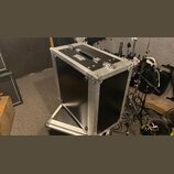 Černý transportní flightcase s hliníkovými hranami a kovovými rohy. Na horní straně je umístěna černá rukojeť a dva kovové zámky, vedle nich je nálep…
