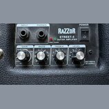 Detailní pohled na ovládací panel kytarového komba s černým texturovaným povrchem. Na panelu je nápis RAZZOR STREET-5 GUITAR AMPLIFIER, vypínač POWER…