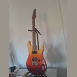 Elektrická kytara s tvarem typu superstrat v přechodovém žluto-červeném odstínu (sunburst). Nástroj má hnědý hmatník, tři černé humbuckery a černý pl…