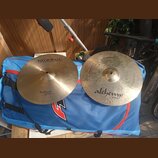 Dvě mosazné činely položené na modrém transportním sáčku. Horní činel nese nápisy „Istanbul Agop“ a „Traditional REGULAR thin“. Dolní činel má nápis…