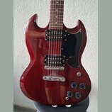 Tmavě červená elektrická kytara s hnědým hmatníkem a černým pickguardem. Nástroj je vybaven dvěma humbuckery, stříbrným mostem a čtyřmi černými ováln…