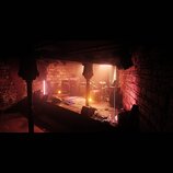 Fotografie zachycuje osvětlené pódium v prostoru s cihlovými stěnami. Na scéně je umístěna bicí souprava, několik kytarových komb a monitorů. V pozad…