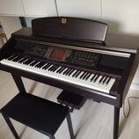 Tmavně hnědý digitální piano s klaviaturou, ovládacím panelem a přívodním kabelem. Na horní části je nápis "KORG Clavinet". Součástí je černá polstro…